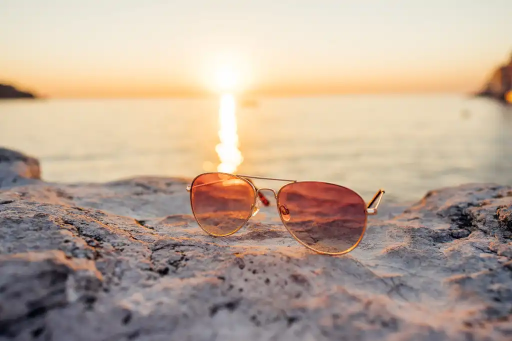 sunglasses on a stone with sun rays during sunset free photo